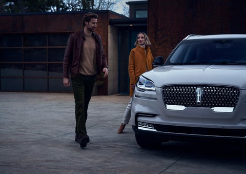 A man and a woman approaching a 2024 Lincoln Aviator® SUV, which illuminates certain lights when they are close | Cogswell Lincoln in Russellville AR